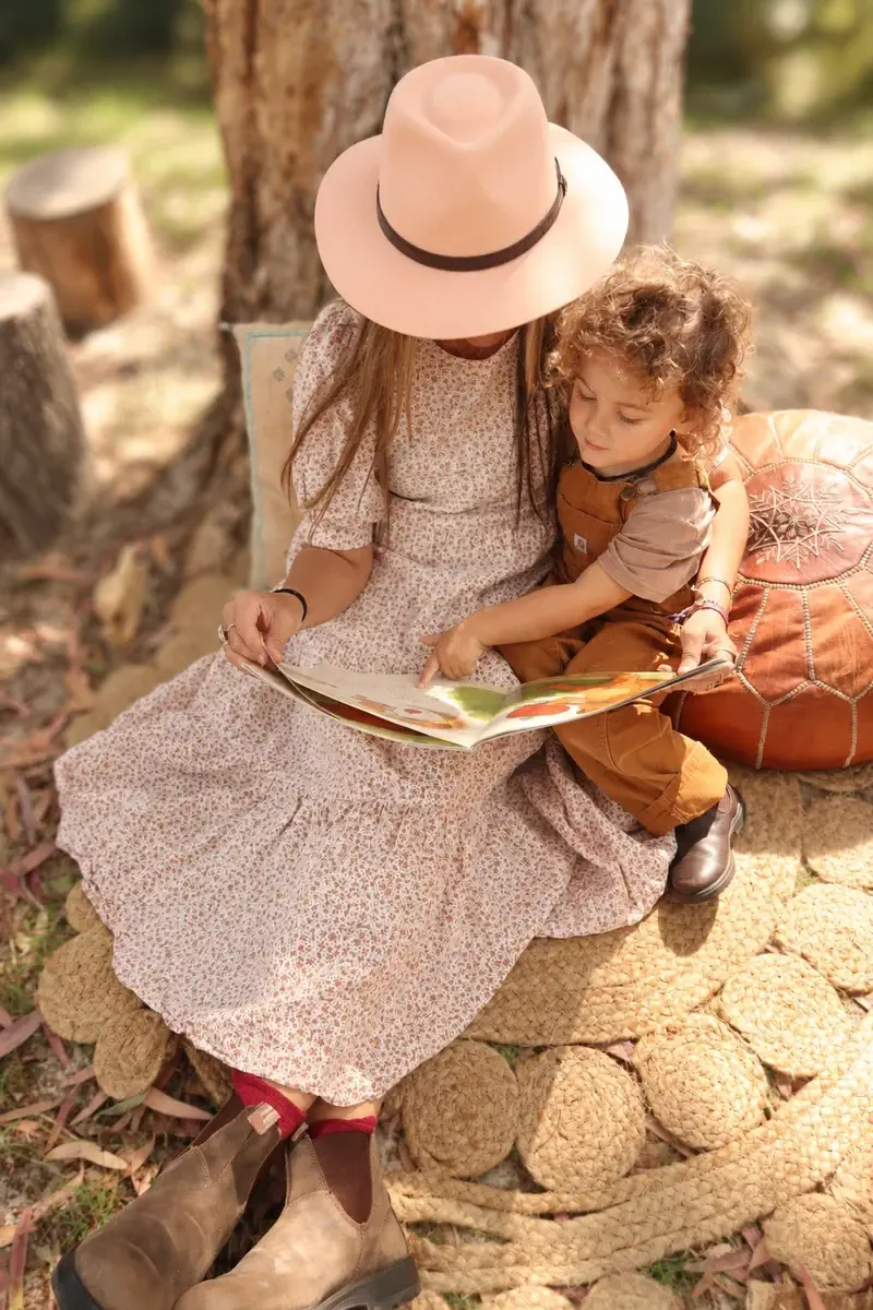 Older child reading a picture book to a toddler under a tree during hygge time at Sunshine Mini School