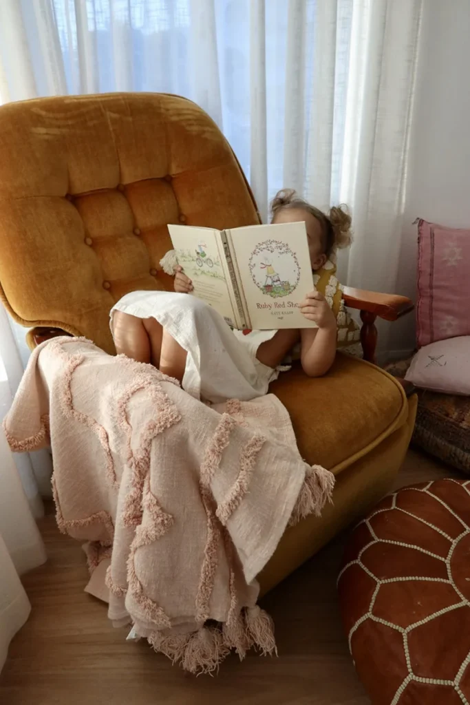Child relaxing with a book in a cosy hygge corner that supports wellbeing in early childhood