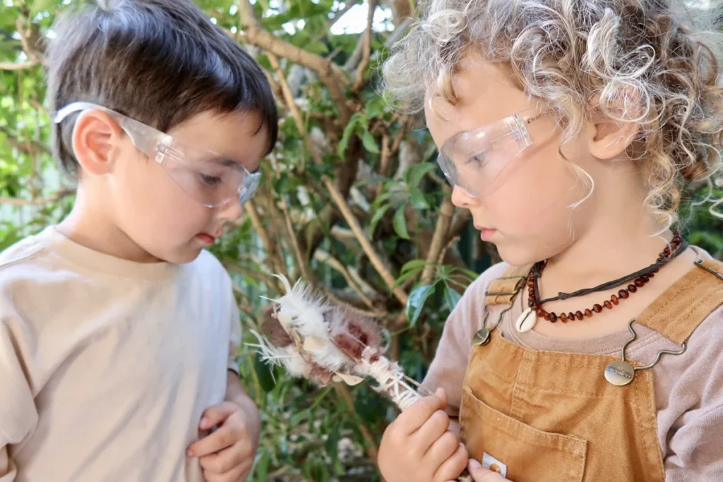 Two preschoolers in safety glasses examining a seed pod during hands-on science play