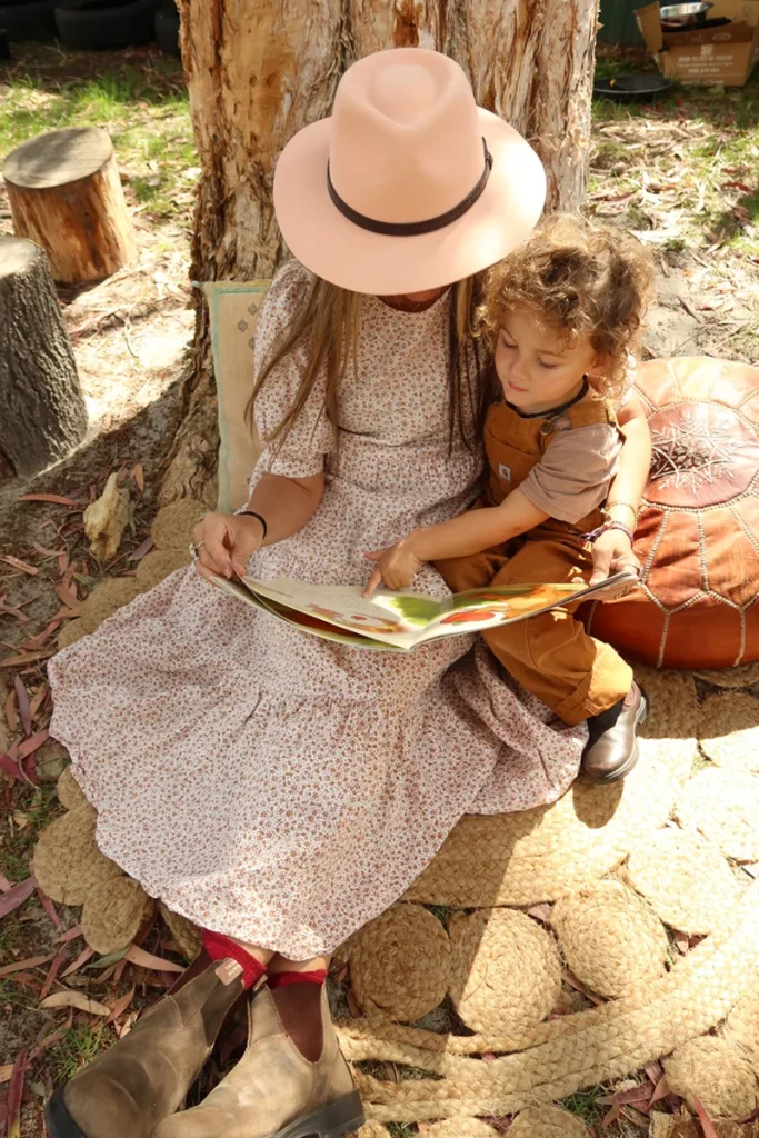 Older child reading to a toddler on a log seat during hygge time at Sunshine Mini School